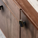 "Black brass circular knob with gold trim on a brown wooden cabinet."