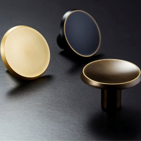 "Three circular brass knobs in gold, black, and bronze with concave surface and chamfered edges."