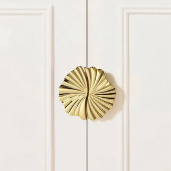 "A gold brass fan-shaped drawer pull mounted on a white cabinet."