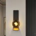 Modern wall lamp with black metal frame and smoky glass globe casting warm light on white wall.