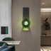 Green spherical wall lamp with black metal mounting plate, illuminated against beige wall in modern interior.