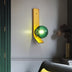 Yellow and green modern wall lamp with spherical green glass shade mounted on white wall above black furniture.