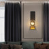 Modern wall sconce with textured glass sphere and brass accent mounted on taupe paneled wall above upholstered headboard.