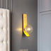 Modern wall lamp with yellow metal bracket and frosted glass globe, mounted on gray wall next to white headboard.