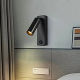 "A modern black bedside reading lamp with an adjustable cylindrical head mounted on a gray wall above a gray headboard."