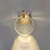 Wall lamp with gold glitter circular shade and pleated fabric base casting warm light against gray background.