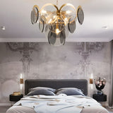 "A modern chandelier with layered smoked glass discs hanging above a bed in a stylish bedroom with patterned wallpaper."