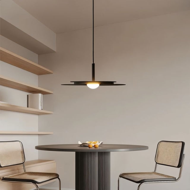 "A modern disc pendant light hanging above a round table in a minimalist dining room."