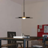 "A disc-shaped pendant light hanging above a wooden dining table with chairs."