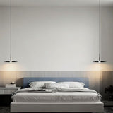 "Two disc-shaped pendant lights hanging on either side of a modern bed in a bedroom."