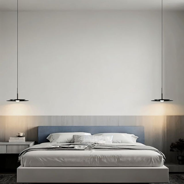 "Two disc-shaped pendant lights hanging on either side of a modern bed in a bedroom."