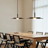 "Two disc-shaped pendant lights hanging above a long wooden dining table with chairs."