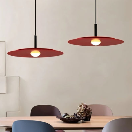 "Two red disc pendant lights hanging above a dining table with chairs."