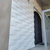 White horizontal brick wall panels with shadow lines installed on exterior wall next to black ornamental door.