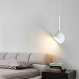 "A white, curved iron pendant light with a dome-shaped shade provides focused illumination for reading in bed, with books stacked on a nightstand."