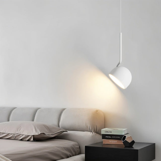 "A white, curved iron pendant light with a dome-shaped shade provides focused illumination for reading in bed, with books stacked on a nightstand."