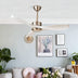 Brushed nickel ceiling fan with curved blades installed above a modern living room with gray sofa and wall art.