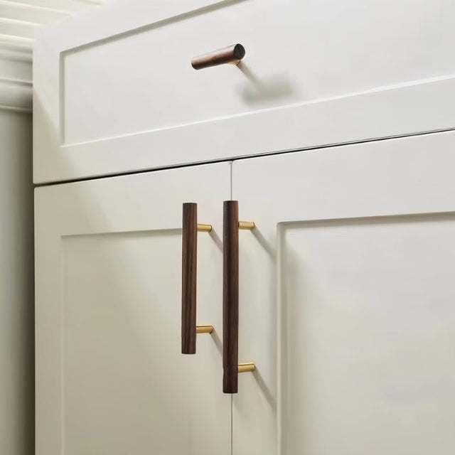 "Modern wooden knobs and pull handles with brass accents on white kitchen cabinets."