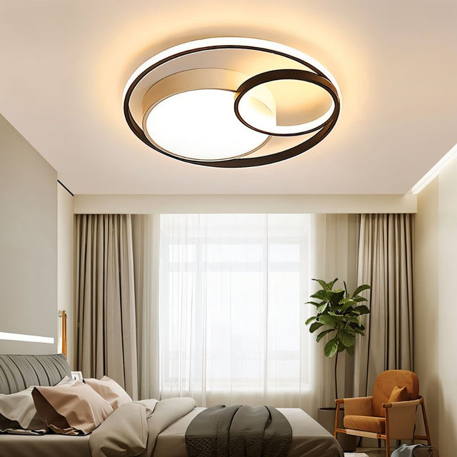 "A modern black ceiling light with interlocking rings in a bedroom with a bed and plant."