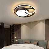 "A modern black ceiling light with interlocking rings in a bedroom with a bed and wall paneling."