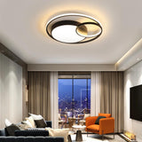 "A modern black ceiling light with interlocking rings in a living room with a blue sofa and orange chair."