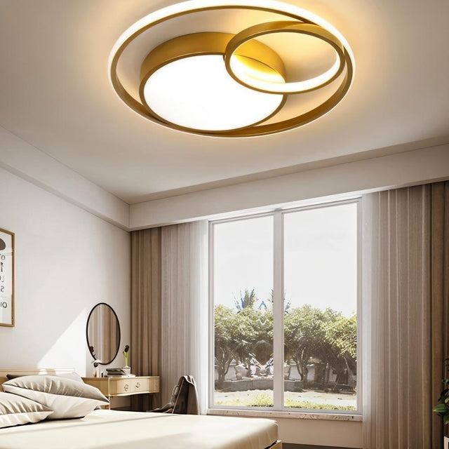 "A modern gold ceiling light with interlocking rings in a bedroom with a large window."