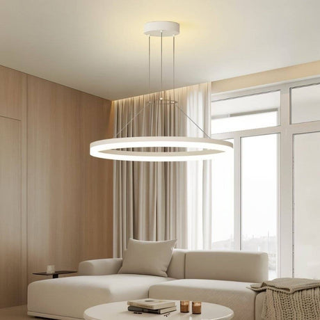 "A modern white ring chandelier in a living room with a white sofa and round table."