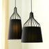 Two black pendant lights with fabric shades and wire frames hang against a cream and beige striped wall.