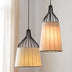 Two black metal pendant lights with cream fabric shades hang against a white wall with sheer curtains.