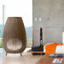 Woven rattan floor lamp with tapered teardrop shape in natural brown finish, displayed in modern bedroom setting.