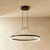 "Black and gold Capli chandelier with dual aluminum rings and acrylic diffusers, hanging above a living room with a beige sofa."