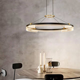 "Black and gold Capli chandelier with dual aluminum rings and acrylic diffusers, hanging above a round dining table with chairs."