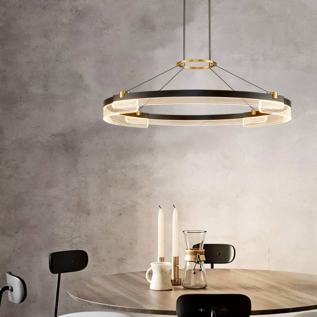 "Black and gold Capli chandelier with dual aluminum rings and acrylic diffusers, hanging above a round dining table with chairs."