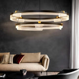 "Black and gold Capli chandelier with dual aluminum rings and acrylic diffusers, hanging above a living room with a beige sofa."