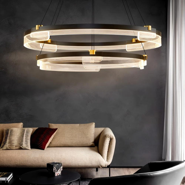 "Black and gold Capli chandelier with dual aluminum rings and acrylic diffusers, hanging above a living room with a beige sofa."