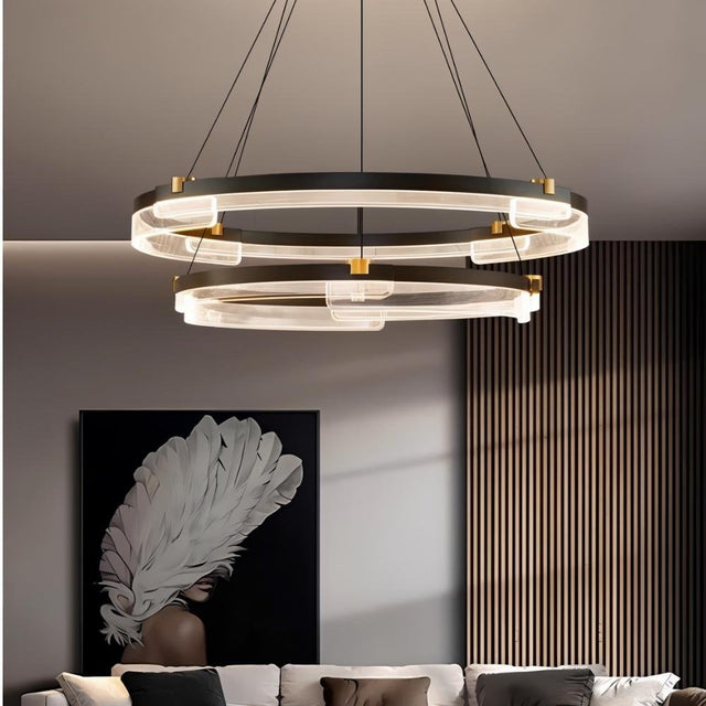 "Black and gold Capli chandelier with dual aluminum rings and acrylic diffusers, hanging above a living room with a modern art piece."