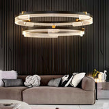 "Black and gold Capli chandelier with dual aluminum rings and acrylic diffusers, hanging above a living room sofa with decorative pillows."