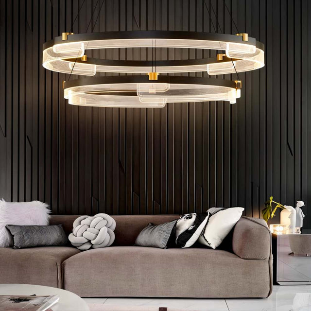 "Black and gold Capli chandelier with dual aluminum rings and acrylic diffusers, hanging above a living room sofa with decorative pillows."