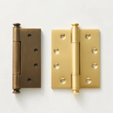 "Two solid brass barrel hinges with decorative finials, one antique and one polished, shown on a light background."