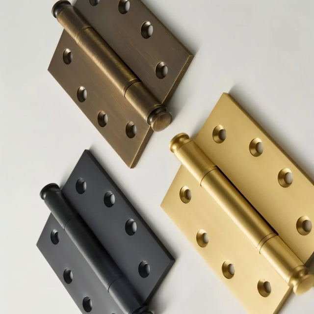 "Close-up of three solid brass barrel hinges with decorative finials in antique, black, and polished finishes."
