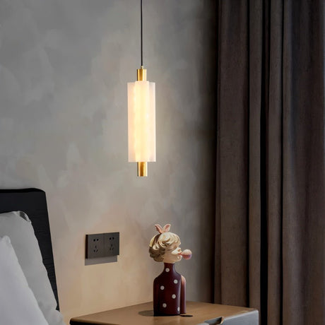 "A minimalist pendant light with a frosted acrylic cylinder and brass accents hanging in a modern bedroom."