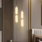 "Two minimalist pendant lights with frosted acrylic cylinders and brass accents, hanging in a modern space."