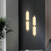 "Two minimalist pendant lights with frosted acrylic and brass, illuminating a modern living room with a gray accent wall."