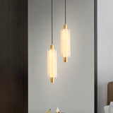 "Two minimalist pendant lights with frosted acrylic cylinders and brass accents, hanging in a modern space."
