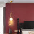 Gold pendant light with frosted globe shade hanging in burgundy bedroom above bedside table.