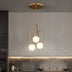 Gold brass pendant light with three frosted white spherical shades hanging above a modern kitchen counter.
