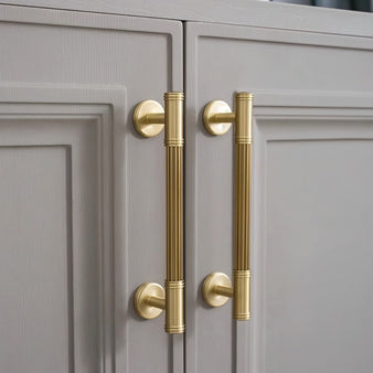 "Two sleek brass pull bars with grooved detailing mounted on a gray shaker-style cabinet, adding a sophisticated touch to a classic kitchen design."