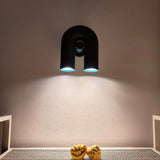 "A black, contemporary wall lamp with a looped design, casting a blue-tinted light on a textured gray wall."