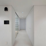 "A black, contemporary wall lamp with a looped design, mounted on a white wall in a minimalist hallway."