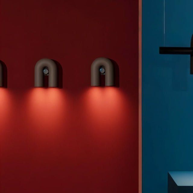 "Three black, contemporary wall lamps with a looped design, mounted on a vibrant red wall, emitting a warm glow."